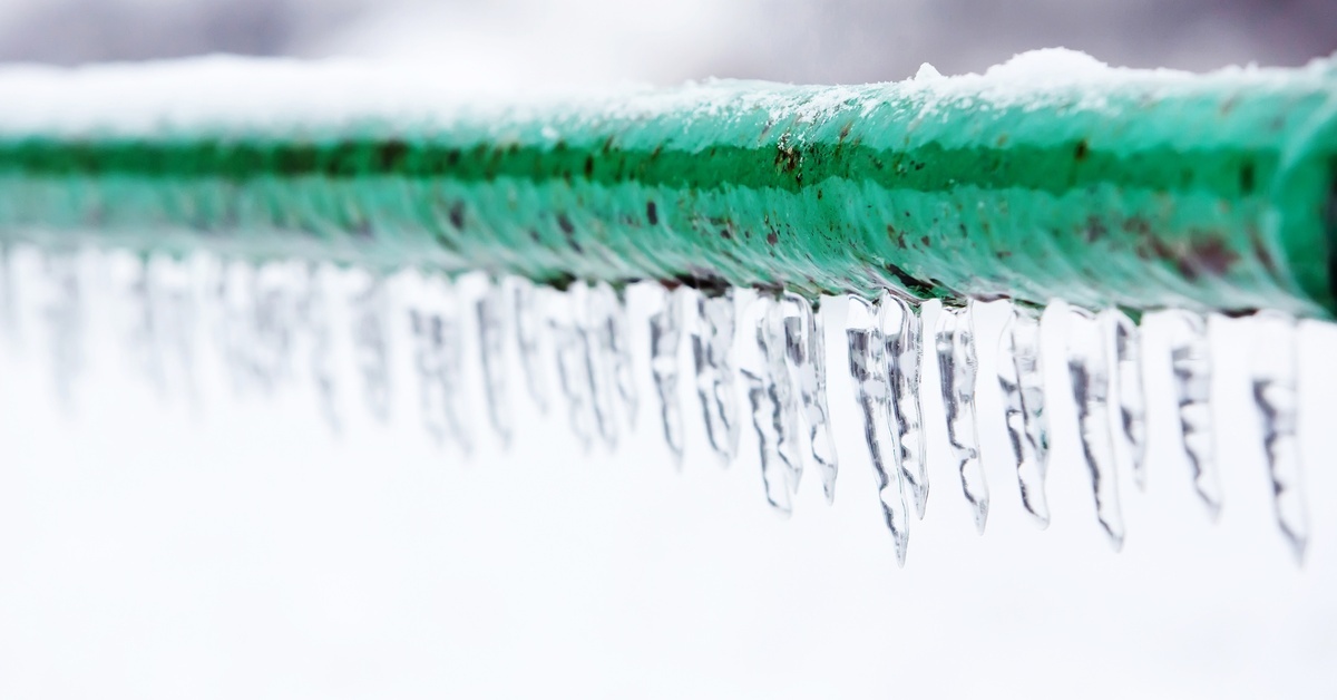 An extreme close-up of a green, rusty pipe that's frozen over with icicles and water. There's a bit of snow on top.