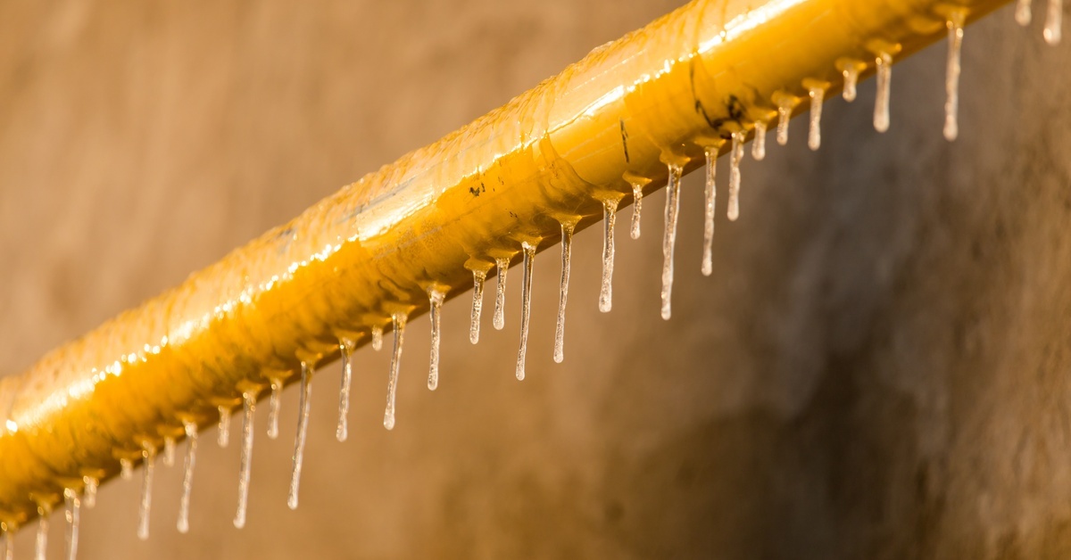 A close-up of small icicles frozen solid on a yellow pipe in a concrete industrial building at sunset.