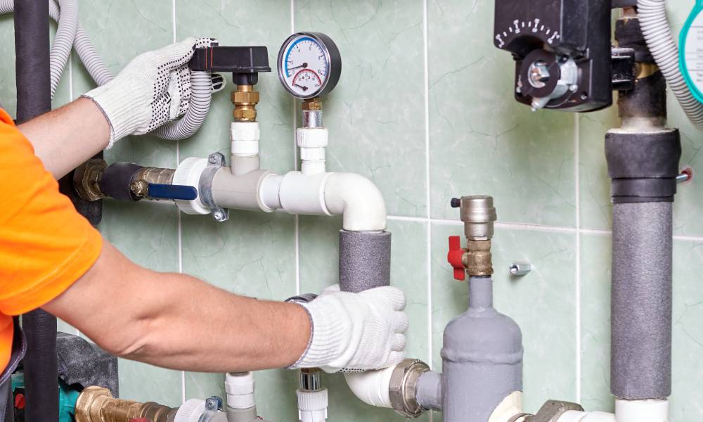 A person in an orange shirt and white gloves checks the operation of a water heater system by moving a valve.