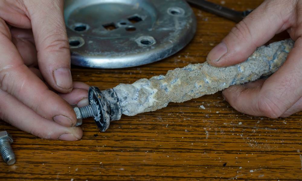 A person’s hands hold a small water heater component that is crusted and clogged with sediment buildup.