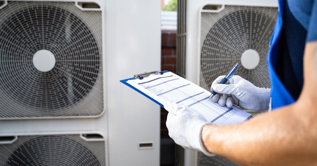A person in white gloves standing next to several air conditioning units. They are holding a clipboard with papers on it.