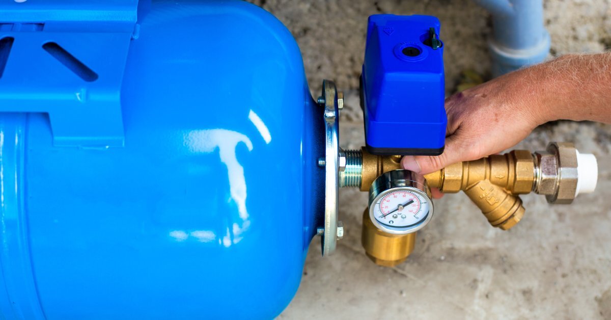 A person’s hand reaches forward and uses a pressure gauge to measure the water pressure inside a bright blue water tank.