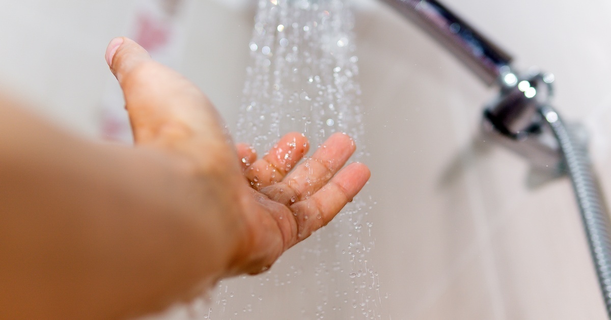A person’s hand reaching out to test the stream of water coming from the shower faucet. Water flows in a trickle.