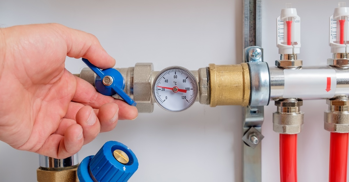 A pressure valve installed on a series of plumbing pipes. A person’s hand is reaching forward to adjust the valve.