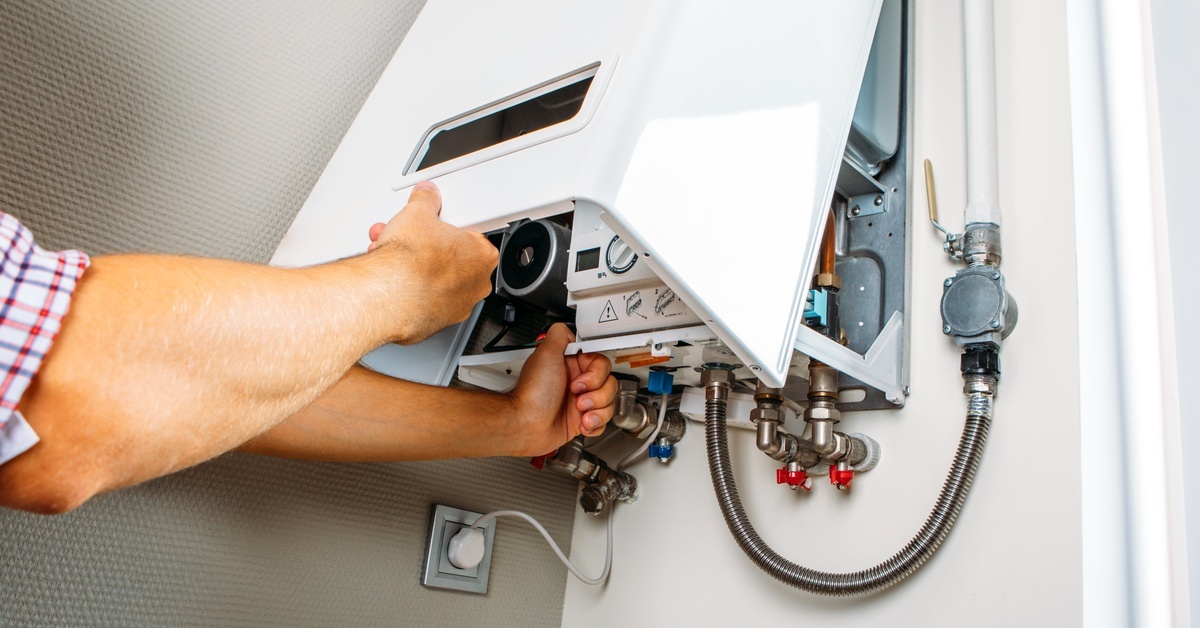 A man lifting up the casing of a heating unit. There are several valves located under the heating unit.