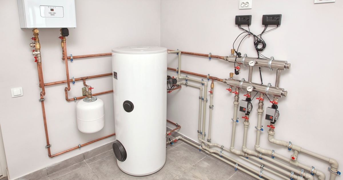 A boiler room features several intricate pipes leading to a hot water boiler and a wall-hung water heater.