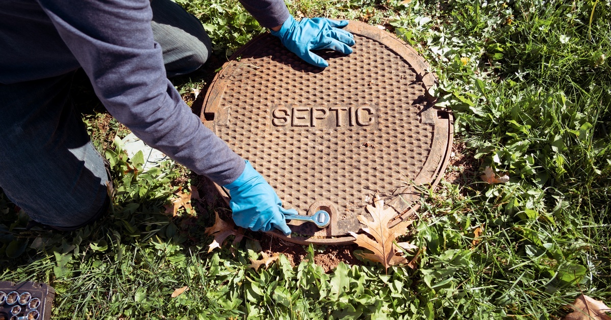A person wearing blue gloves is touching a metal cover. The cover is on a grassy patch of ground.