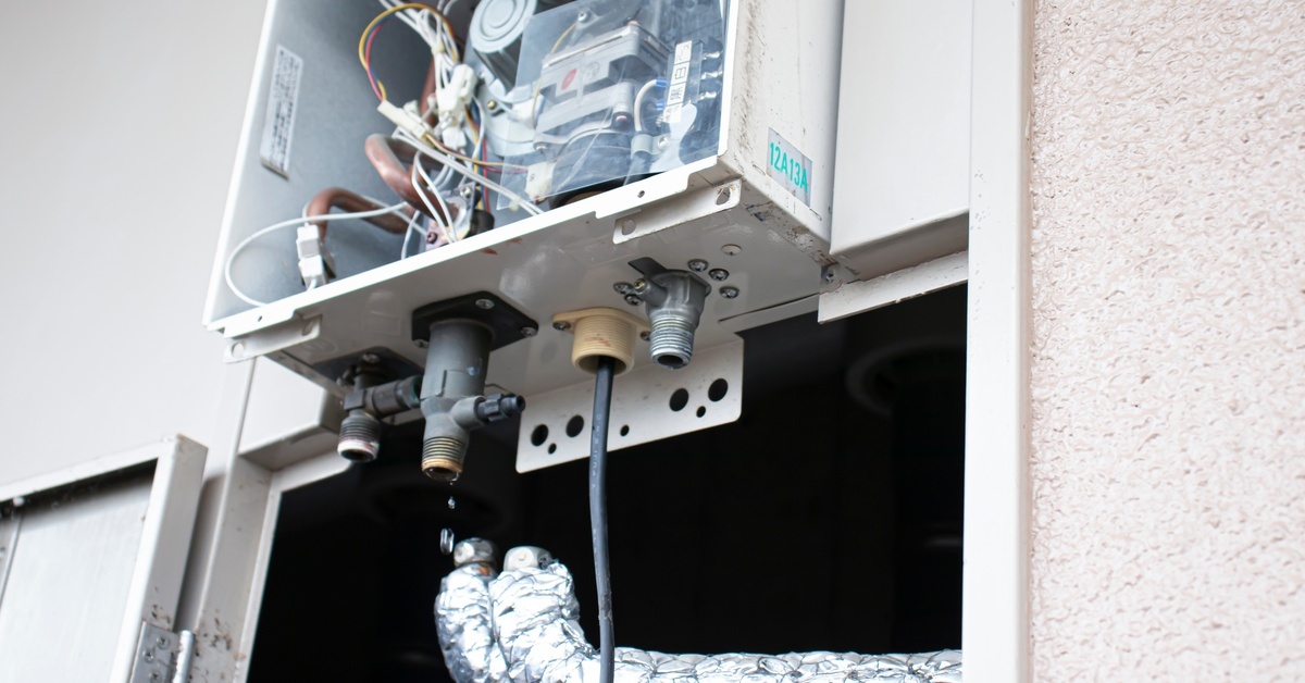 An outdoor tankless water heater with its internal components exposed, including its piping covered in insulation.