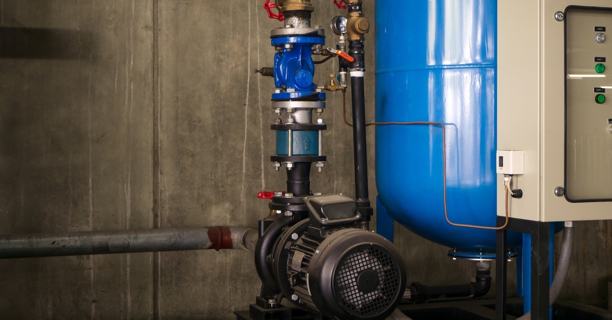 Noise Reduction Strategies for Urban Booster Pump Installs A water booster pump system connected to a set of silver pipes on one side and a blue tank on the other.